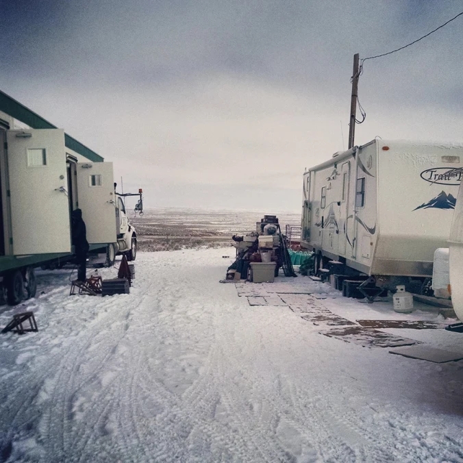 Image shows two mobile trailers here researchers stayed, parked in an open field covered with snow, ice, and mud.